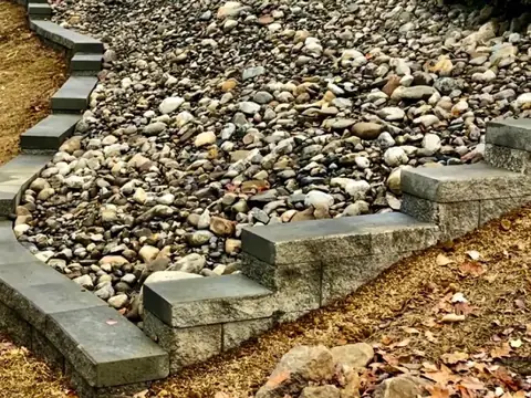 A bed of rounded river rock running down a slope between low capped block steps