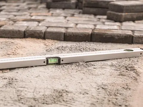 A spirit level lying on a bed of screeded sand, with concrete pavers laid behind it