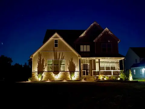 A two-story house after dark, with low lights shining up its stone base and the planting along its front