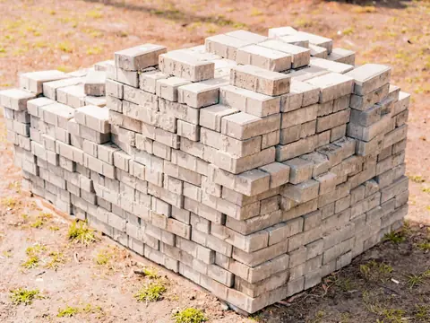 Gray concrete pavers stacked on a pallet on bare ground