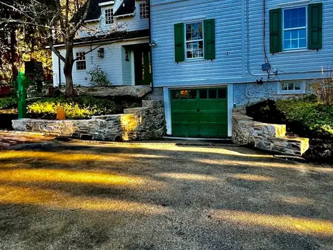 Natural fieldstone walls on both sides of a garage entrance, below a white house with green shutters