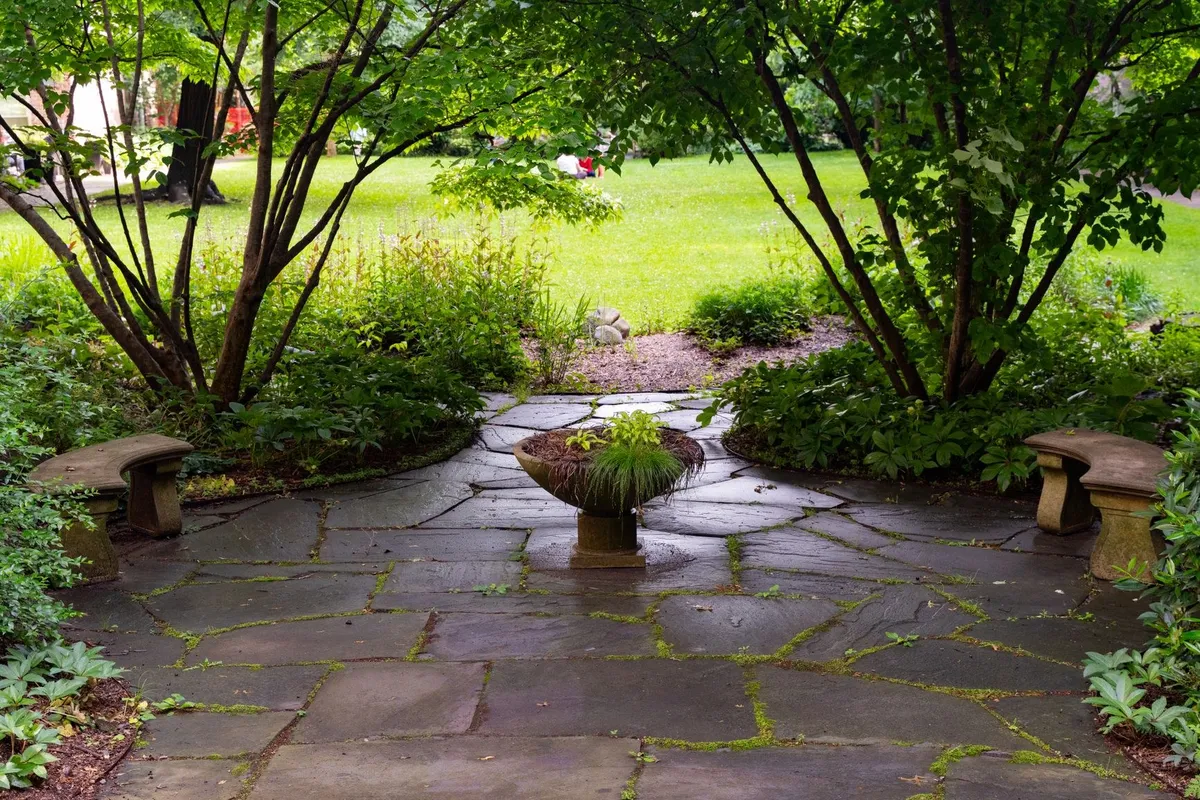 A serene stone patio surrounded by lush greenery and a central plant, ideal for small yard design.